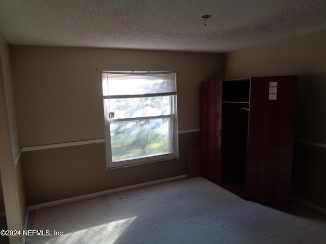 unfurnished bedroom with light colored carpet, a textured ceiling, and a closet