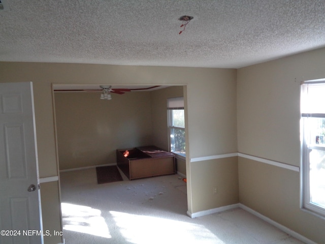 empty room with ceiling fan, carpet, a healthy amount of sunlight, and a textured ceiling