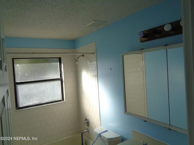 bathroom featuring toilet, a textured ceiling, and tiled shower / bath