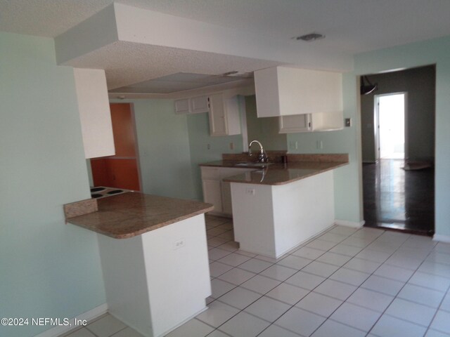 kitchen with kitchen peninsula, light tile patterned floors, white cabinets, and sink