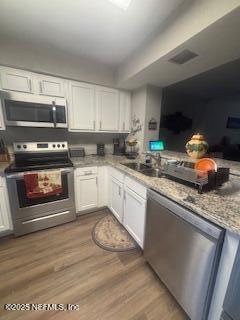 kitchen featuring stainless steel appliances, light stone countertops, hardwood / wood-style floors, and white cabinets