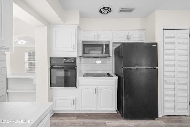 kitchen featuring white cabinets, decorative backsplash, light wood-type flooring, and black appliances