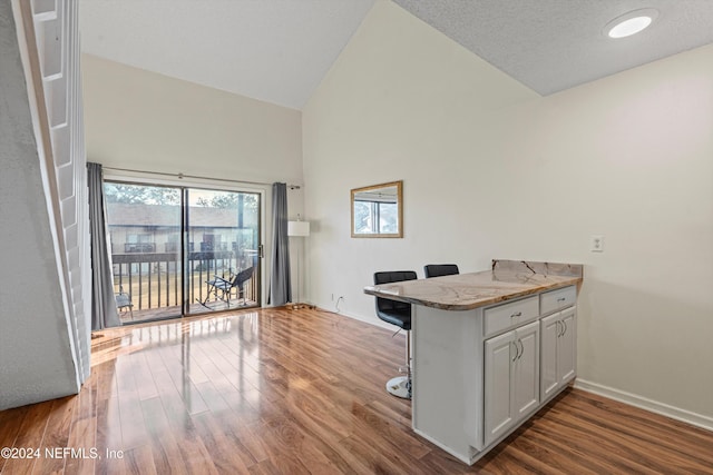 kitchen featuring white cabinets, a breakfast bar, light stone counters, and hardwood / wood-style floors