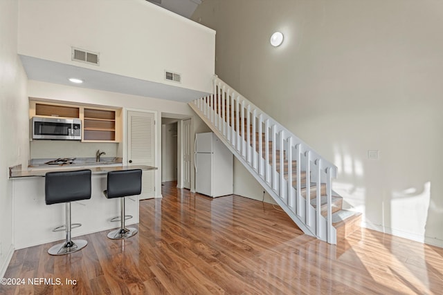 kitchen with a high ceiling, a kitchen breakfast bar, kitchen peninsula, hardwood / wood-style floors, and white fridge