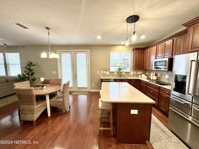 kitchen featuring appliances with stainless steel finishes, a center island, hanging light fixtures, and dark wood-type flooring