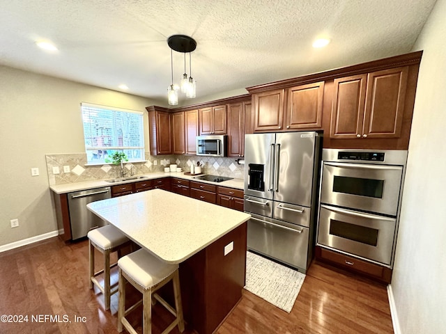 kitchen featuring appliances with stainless steel finishes, sink, decorative light fixtures, a center island, and dark hardwood / wood-style floors