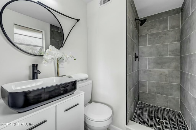 bathroom featuring a tile shower, vanity, and toilet