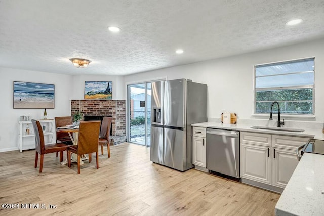 kitchen featuring sink, stainless steel appliances, a textured ceiling, white cabinets, and light wood-type flooring