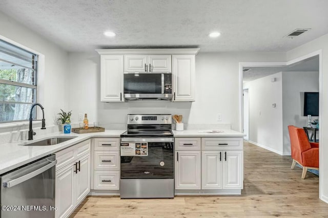 kitchen with sink, white cabinetry, stainless steel appliances, and light hardwood / wood-style flooring