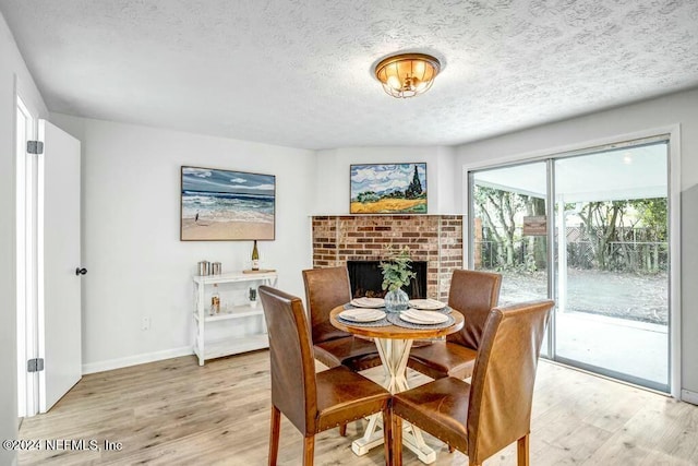 dining area with a brick fireplace, a textured ceiling, and light hardwood / wood-style flooring