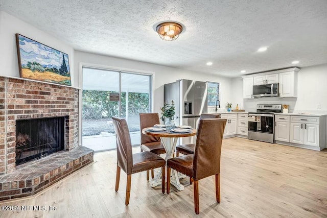 dining room with a textured ceiling, light hardwood / wood-style floors, sink, and a fireplace