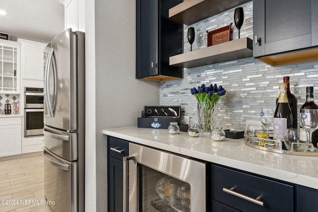 kitchen featuring appliances with stainless steel finishes, tasteful backsplash, wine cooler, white cabinets, and light stone countertops