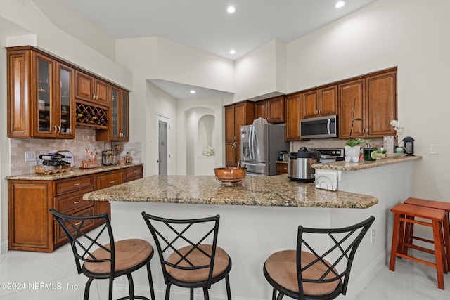 kitchen featuring kitchen peninsula, a kitchen breakfast bar, backsplash, light stone counters, and stainless steel appliances