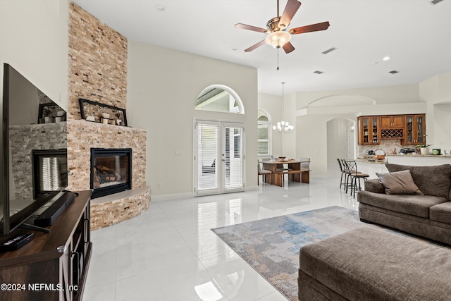 living room featuring french doors, a towering ceiling, a fireplace, light tile patterned flooring, and ceiling fan with notable chandelier