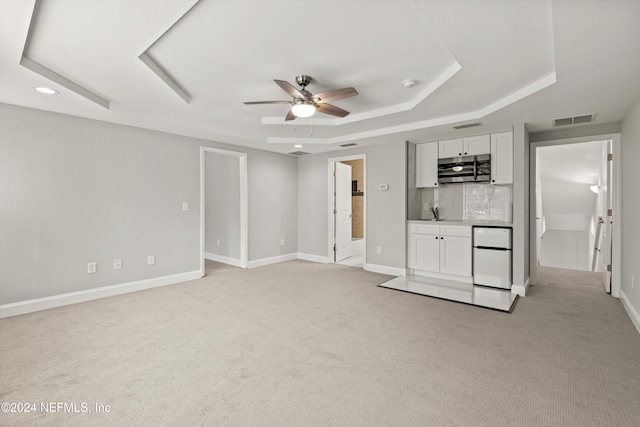 unfurnished living room featuring a tray ceiling, ceiling fan, and light colored carpet