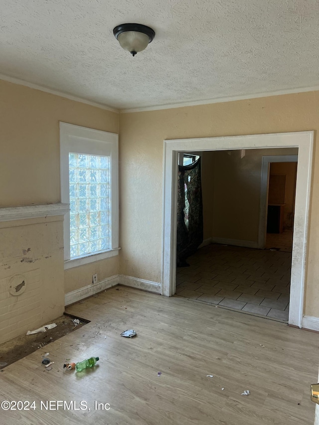 empty room featuring light hardwood / wood-style floors, ornamental molding, and a textured ceiling