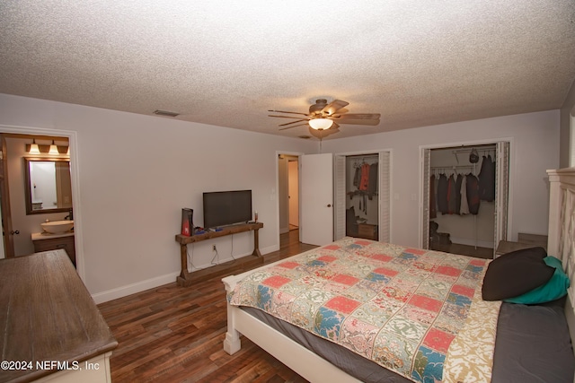 bedroom featuring two closets, ensuite bath, ceiling fan, a textured ceiling, and dark hardwood / wood-style flooring