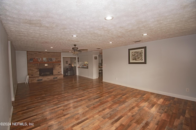 unfurnished living room featuring ceiling fan, a fireplace, dark wood-type flooring, and a textured ceiling