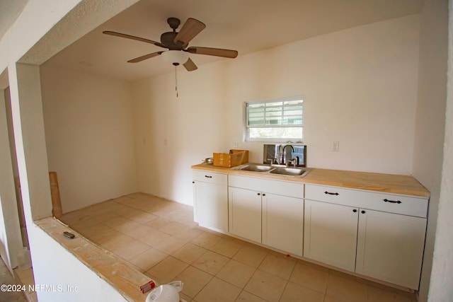 kitchen with wood counters, ceiling fan, sink, light tile patterned floors, and white cabinets