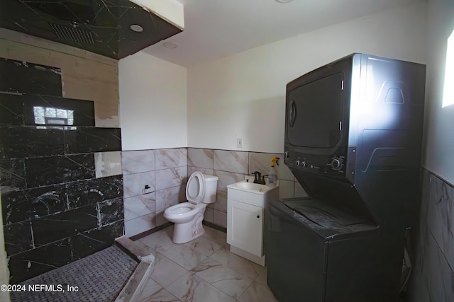 bathroom with stacked washer / dryer, vanity, tile walls, and toilet