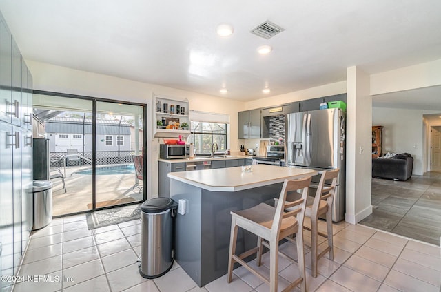 kitchen featuring appliances with stainless steel finishes, gray cabinetry, sink, a kitchen island, and light tile patterned flooring