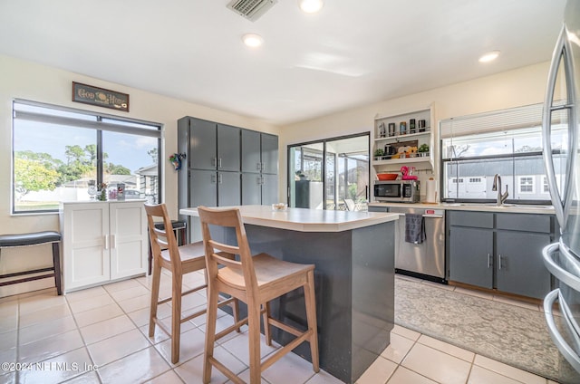 kitchen featuring sink, a center island, gray cabinets, light tile patterned flooring, and appliances with stainless steel finishes