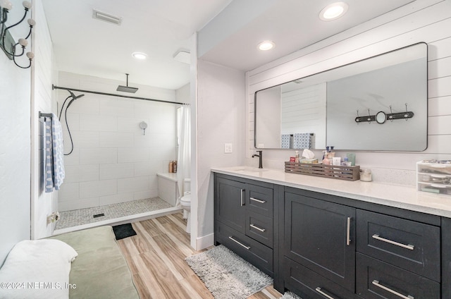 bathroom featuring a tile shower, toilet, vanity, and hardwood / wood-style flooring