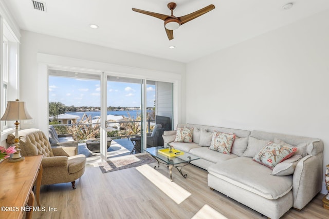 living room with light hardwood / wood-style floors, ceiling fan, and a water view