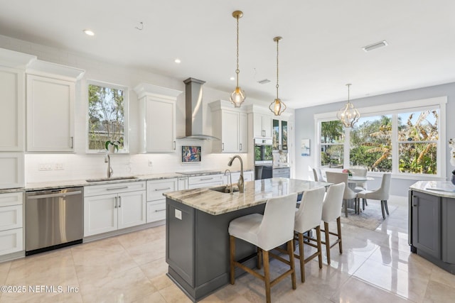 kitchen with pendant lighting, dishwasher, sink, wall chimney range hood, and a center island with sink