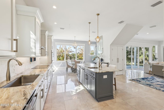 kitchen featuring pendant lighting, sink, white cabinets, and a center island with sink