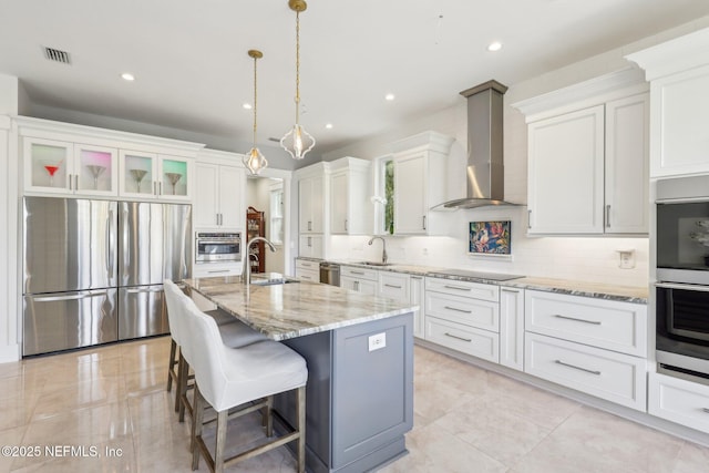 kitchen featuring white cabinetry, wall chimney range hood, a center island with sink, and appliances with stainless steel finishes