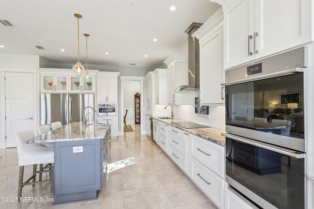 kitchen featuring hanging light fixtures, a kitchen island with sink, wall chimney range hood, and white cabinets