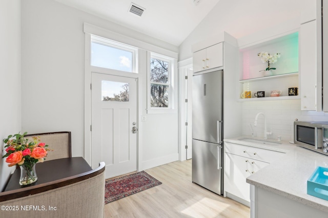 kitchen featuring lofted ceiling, sink, appliances with stainless steel finishes, backsplash, and white cabinets