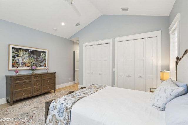 bedroom with lofted ceiling, light hardwood / wood-style flooring, and two closets