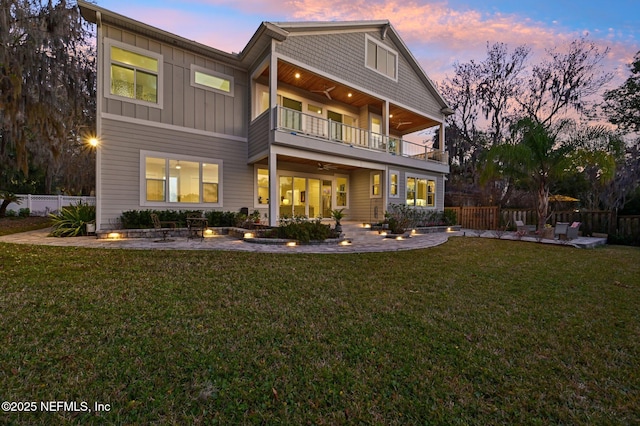 back house at dusk featuring a balcony and a lawn