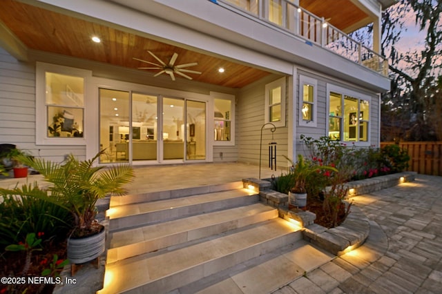 exterior entry at dusk with a patio area, a balcony, and ceiling fan