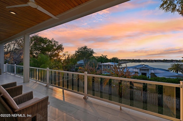 balcony at dusk with a water view and ceiling fan