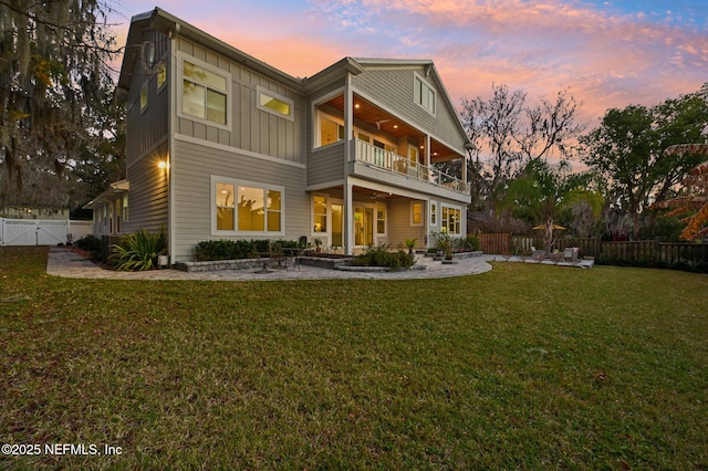 back house at dusk featuring ceiling fan, a yard, a patio, and a balcony