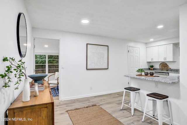 kitchen featuring light hardwood / wood-style floors, light stone countertops, white cabinetry, and a breakfast bar area