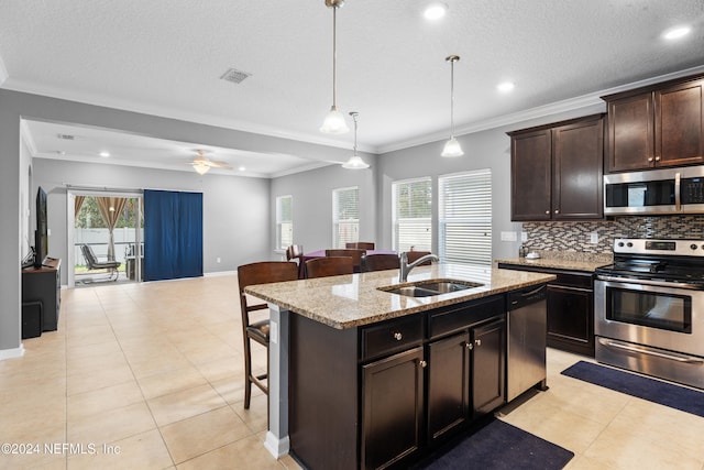 kitchen with a kitchen island with sink, hanging light fixtures, sink, ornamental molding, and stainless steel appliances