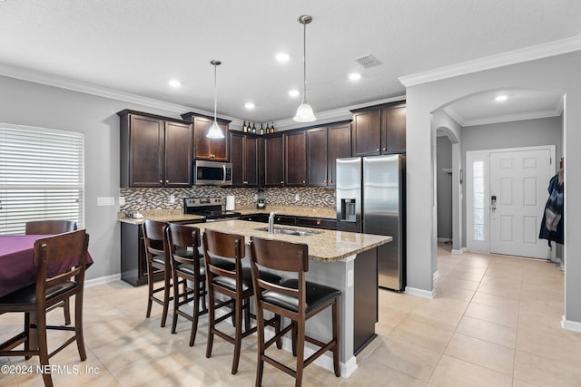 kitchen featuring appliances with stainless steel finishes, dark brown cabinets, crown molding, and an island with sink