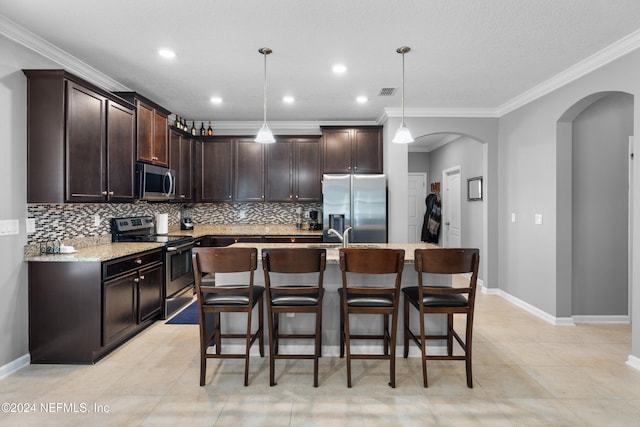 kitchen featuring dark brown cabinetry, an island with sink, pendant lighting, appliances with stainless steel finishes, and ornamental molding