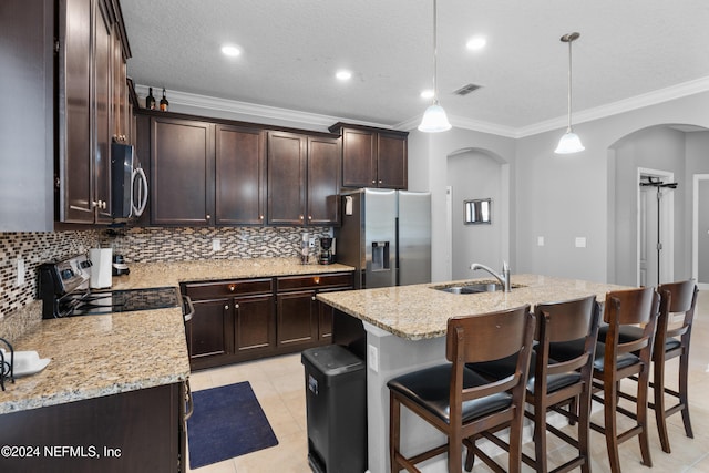 kitchen with sink, stainless steel appliances, an island with sink, pendant lighting, and ornamental molding