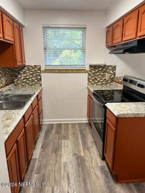 kitchen with light stone countertops, backsplash, sink, hardwood / wood-style floors, and stainless steel range with electric cooktop