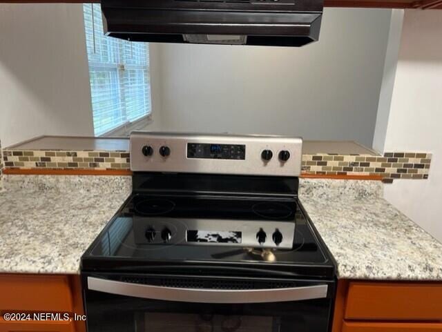 kitchen with stainless steel electric range, light stone counters, decorative backsplash, and exhaust hood