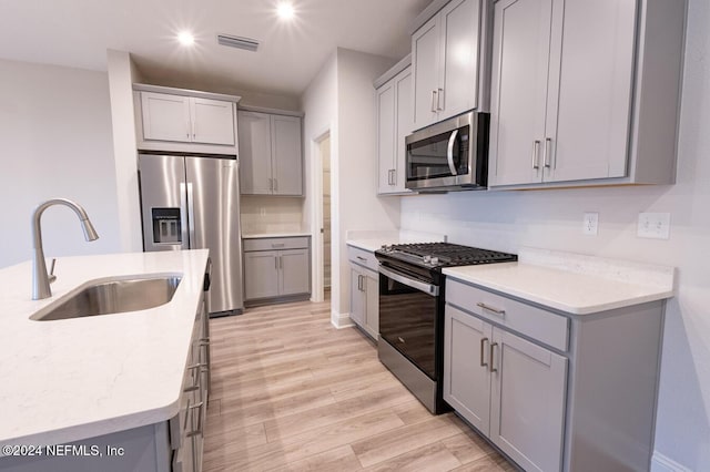 kitchen featuring sink, stainless steel appliances, light stone counters, light hardwood / wood-style floors, and gray cabinets