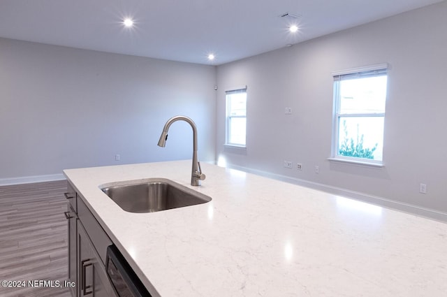 kitchen featuring hardwood / wood-style flooring, light stone counters, plenty of natural light, and sink