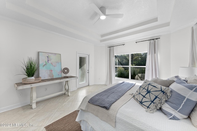 bedroom with a textured ceiling, a tray ceiling, ceiling fan, crown molding, and light tile patterned floors