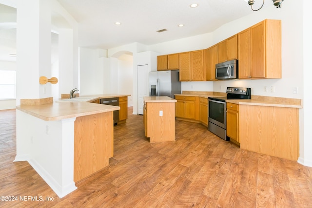 kitchen with kitchen peninsula, stainless steel appliances, sink, light hardwood / wood-style flooring, and a center island