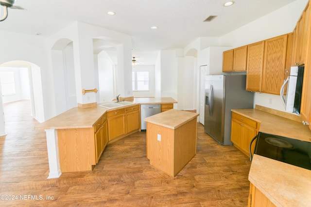 kitchen featuring kitchen peninsula, stainless steel appliances, sink, hardwood / wood-style flooring, and a center island